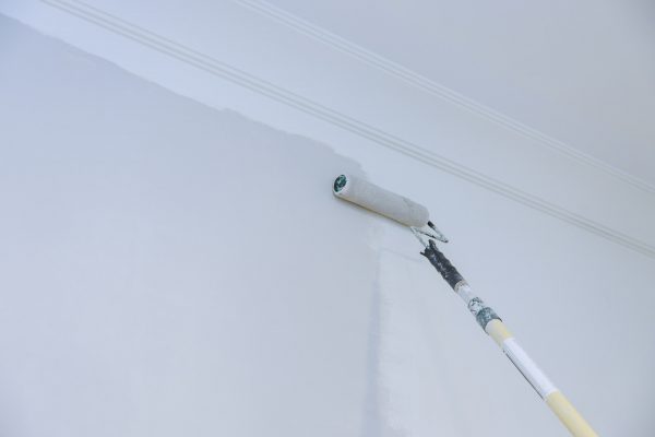 View of painter man painting the wall, with paint roller on empty space