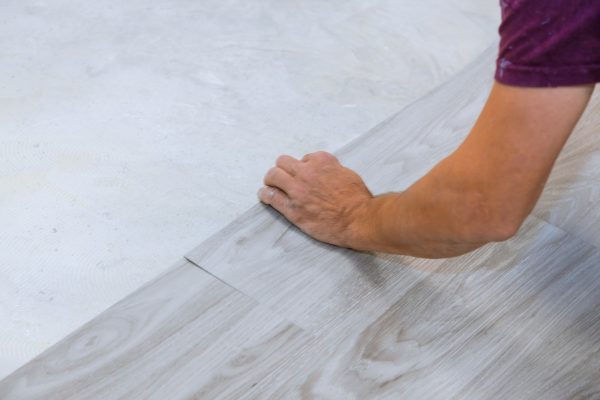 Work on laying worker installing new vinyl tile laminate wood texture floor.